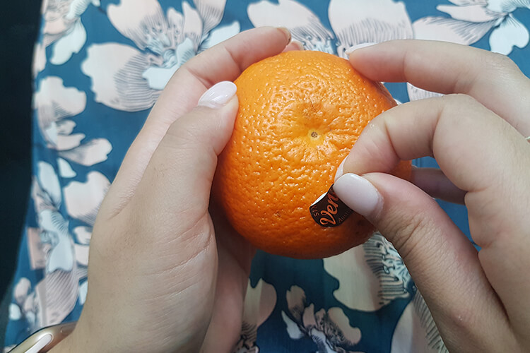 lady peeling a sticker off of an orange